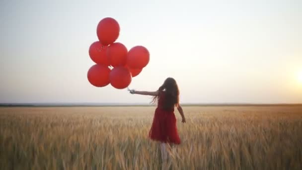 šťastná mladá dívka s balóny, které jsou spuštěny v poli pšenice při západu slunce