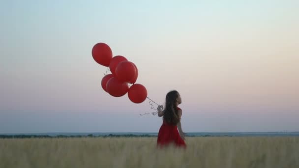 Glad tjej med ballonger som körs i fältet vete vid solnedgången. — Stockvideo