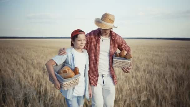 Jóvenes agricultores caminan por el campo de trigo con cestas de pan — Vídeos de Stock