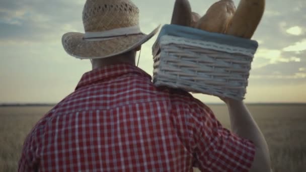 Jovem agricultor está caminhando ao longo do campo de trigo com cestas de pão — Vídeo de Stock