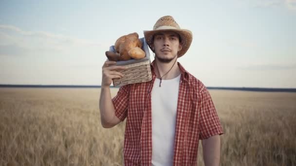 Молодой фермер идет по пшеничному полю с хлебными корзинами — стоковое видео