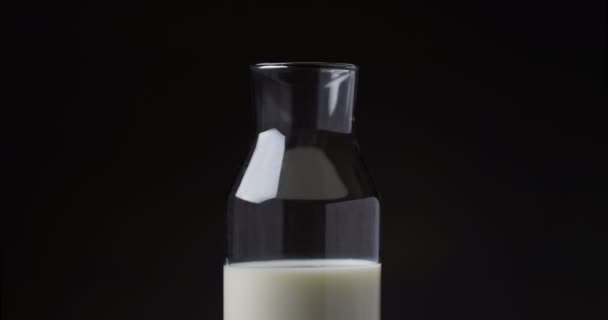 Прекратить движение наполнения стеклянной бутылки молоком на черном фоне — стоковое видео
