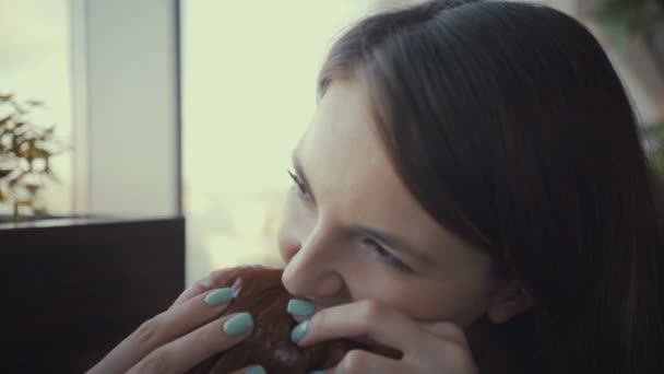 ファーストフードのレストランでおいしいハンバーガーを食べる映像若い女性. — ストック動画