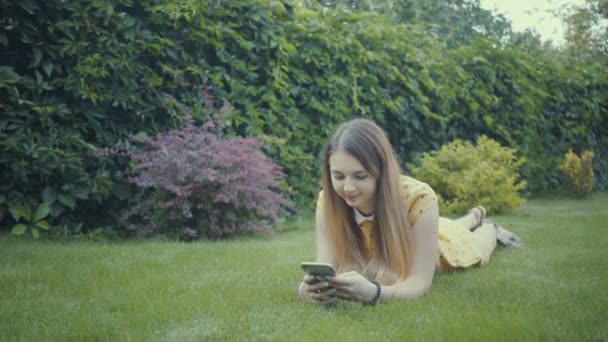 公園の木の近くの彼女のスマート フォンのアプリを使って映像美少女. — ストック動画