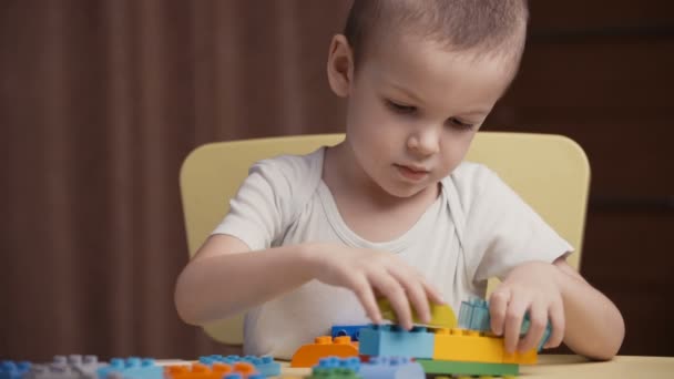 Кадри маленький щасливий хлопчик грає з барвистими блоками конструктора вдома — стокове відео