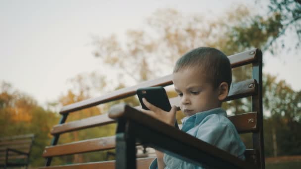 Little boy playing video games on his smartphone outdoors. — Stock Video