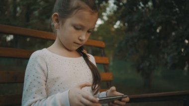 Park ve kullanım smartphone içinde ahşap bir bankta oturan kız öğrenci.