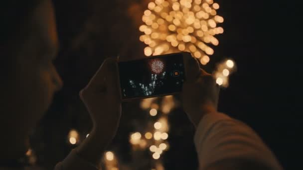 Silueta de una mujer fotografiando fuegos artificiales en el cielo nocturno . — Vídeo de stock