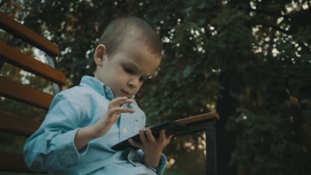 Niño jugando videojuegos en su teléfono inteligente al aire libre . — Vídeo de stock