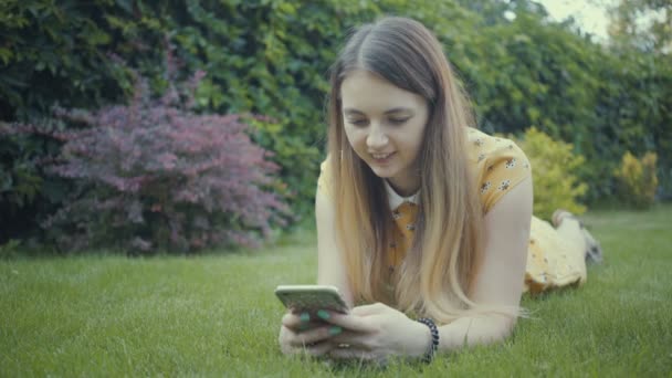 Filmagem menina bonita usando aplicativo em seu smartphone perto da árvore no parque . — Vídeo de Stock