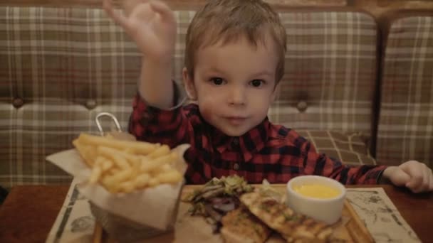 Jongen van twee jaar is het eten van frietjes in een restaurant. — Stockvideo