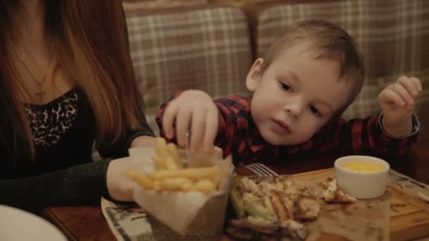 Jongen van twee jaar is het eten van frietjes in een restaurant. — Stockvideo