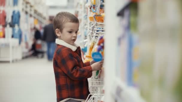 Маленький мальчик стоит в магазине и выбирает игрушки — стоковое видео