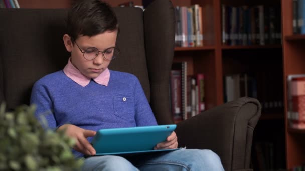 Schattig schooljongen maakt gebruik van de app op zijn smartphone zittend in een stoel — Stockvideo