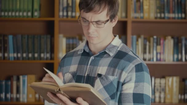 Portret shot van de man die het lezen van een boek in de buurt van de boekenkast in de bibliotheek — Stockvideo