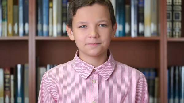 図書館の本棚のそばに立っているかわいい少年の肖像画のショット. — ストック写真