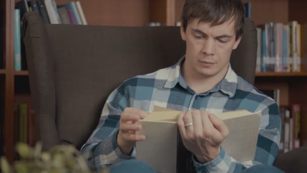 Portret shot van de man die het lezen van een boek in de buurt van de boekenkast in de bibliotheek — Stockvideo