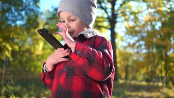 Pojke spelar spelet på smartphone i höst park. — Stockvideo