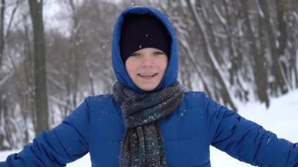 Портрет молодого парня, хлопающего в ладоши снегом в зимнем лесу — стоковое видео