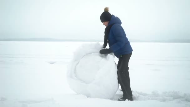 Garçon roule grosse boule de neige pour bonhomme de neige en hiver . — Video
