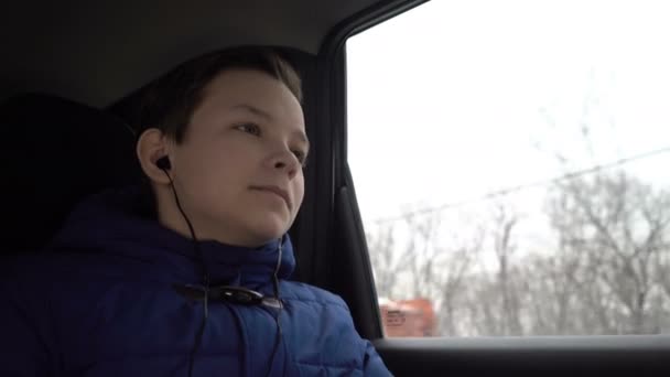 Мальчик-подросток едет на заднем сиденье машины и слушает музыку в наушниках — стоковое видео