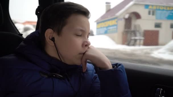 Мальчик-подросток едет на заднем сиденье машины и слушает музыку в наушниках — стоковое видео