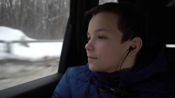 十代の少年、車の後部座席に乗るし、ヘッドフォンで音楽を聴く — ストック動画