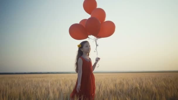 Niña feliz con globos corriendo en el campo de trigo al atardecer. Vídeo 4k . — Vídeos de Stock