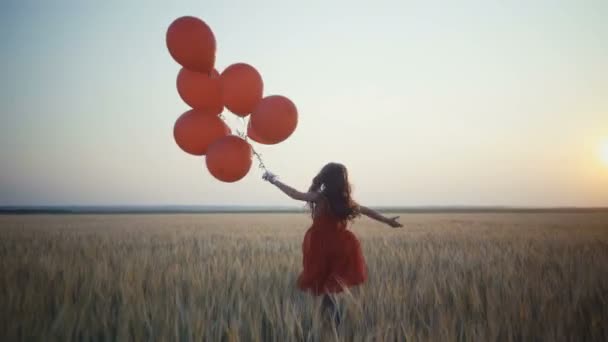 Szczęśliwa młoda dziewczyna z balonów, uruchomiona w polu pszenicy o zachodzie słońca. wideo 4k. — Wideo stockowe