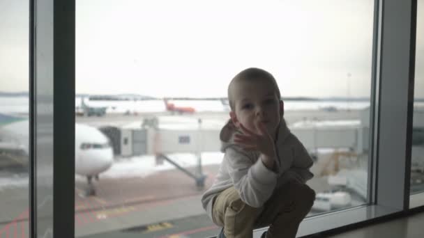 小さな男の子は空港ターミナルの窓に座って、飛行機に乗るのを待っています — ストック動画