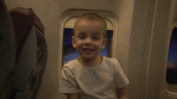 Πορτρέτο του χαριτωμένο αστείο παιδί στο παράθυρο του αεροπλάνου με το ηλιοβασίλεμα μέσα από αυτό στο παρασκήνιο — Αρχείο Βίντεο