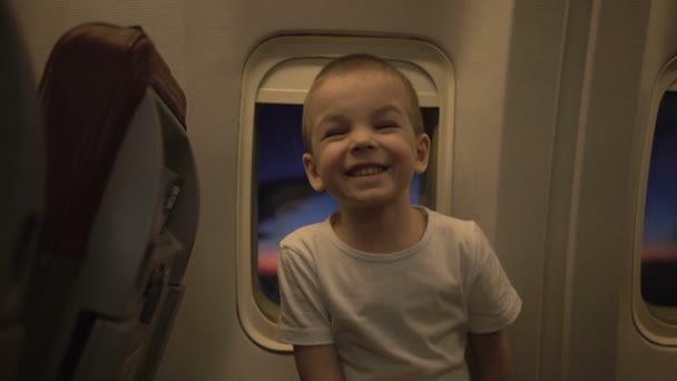Πορτρέτο του χαριτωμένο αστείο παιδί στο παράθυρο του αεροπλάνου με το ηλιοβασίλεμα μέσα από αυτό στο παρασκήνιο — Αρχείο Βίντεο