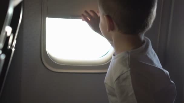 若いかわいい男の子が座席に座って、飛行機の窓を開きます — ストック動画