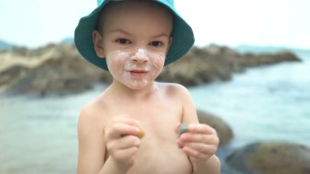 Χαριτωμένο αγόρι με αντηλιακό κρέμα σε ένα ψάθινο καπέλο στην παραλία — Αρχείο Βίντεο