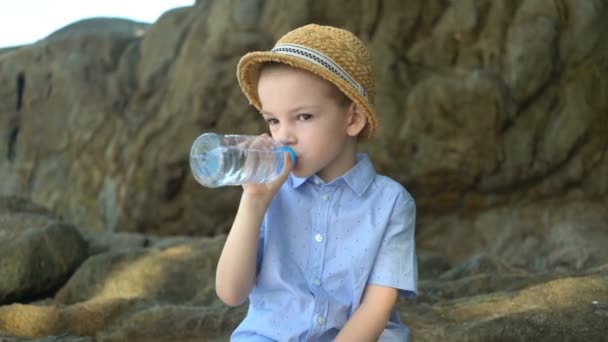 Hezký chlapec pije čistou vodu z plastové láhve za slunného dne. — Stock video