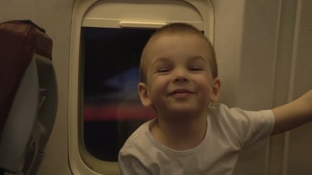 Portrait of cute funny kid at airplane window with sunset through it in background — Stock Video