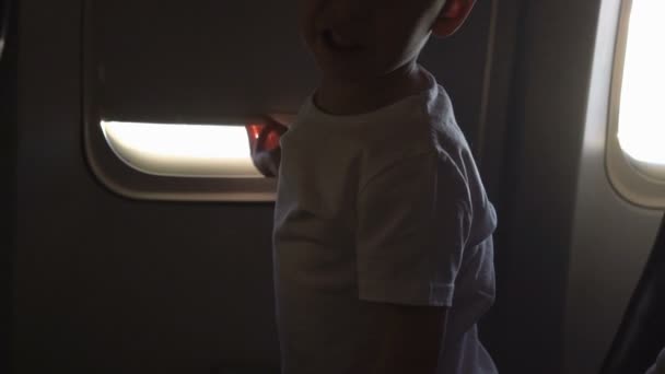 Jeune garçon mignon assis sur le siège et ouvre la fenêtre de l'avion — Video