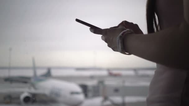 Kobieta za pomocą telefonu komórkowego w terminalu lotniska i czekając na pokład samolotu — Wideo stockowe