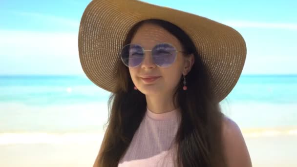 Портрет красивой молодой женщины в шляпе и солнечных очках на пляже — стоковое видео