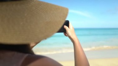 Şapkalı genç gezgin kadın, Ocean Beach 'te akıllı telefondan fotoğraf çekiyor.