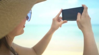 Şapkalı genç gezgin kadın, Ocean Beach 'te akıllı telefondan fotoğraf çekiyor.