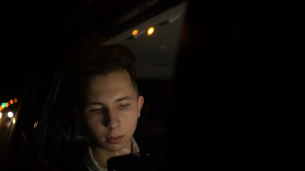 Tiener met behulp van app op zijn telefoon op Late Night op achterbank van de auto — Stockvideo