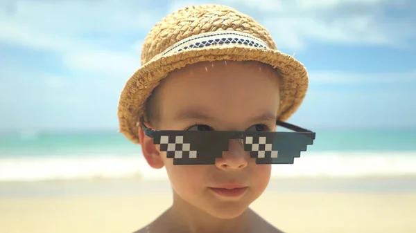 Retrato de lindo niño en sombrero de paja con gafas de sol de pie en la playa de verano — Foto de Stock