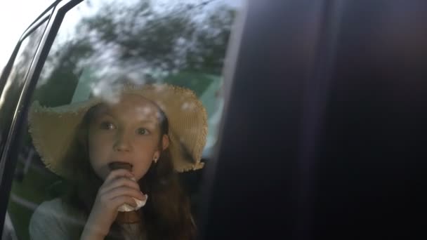 Niña bonita comiendo rosquillas de chocolate en el asiento trasero del coche. concepto de viaje por carretera — Vídeos de Stock