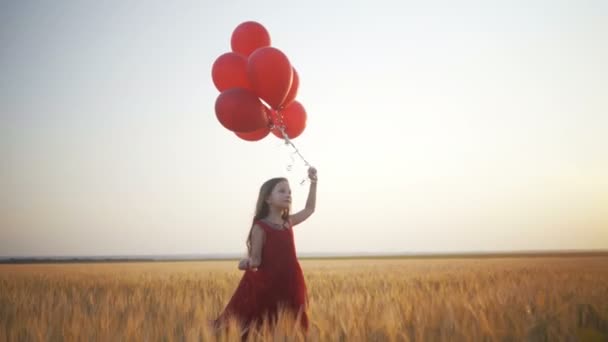 Glad ung flicka med ballonger som körs i fältet vete vid solnedgången — Stockvideo