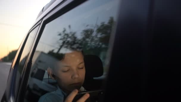 Tonåring med hörlurar inuti bilen tittar på film på smartphone — Stockvideo