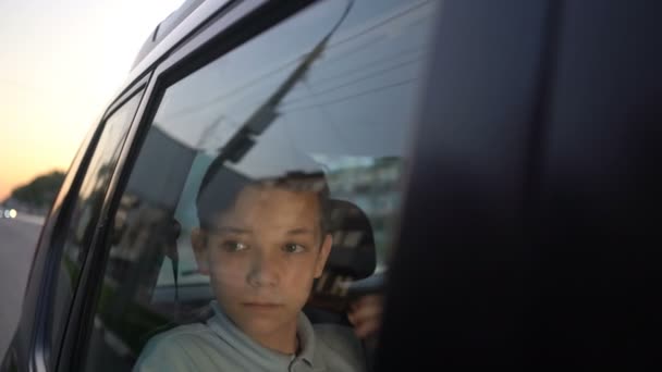 Menino adolescente com fones de ouvido ouvindo a música no banco de trás do carro e olhando para longe — Vídeo de Stock