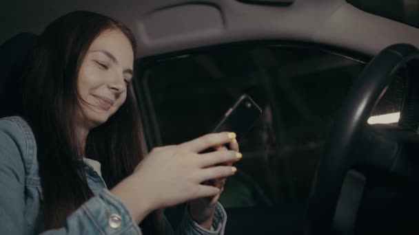 女性は駐車場の車に座っている間に携帯電話でアプリケーションを使用します — ストック動画