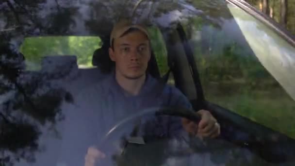 Jonge man kijkt rond rijden auto langs bos kant op zomerdag. — Stockvideo