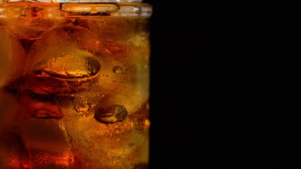 Cola με πάγο και φυσαλίδες σε γυαλί περιστροφή σε μαύρο — Αρχείο Βίντεο